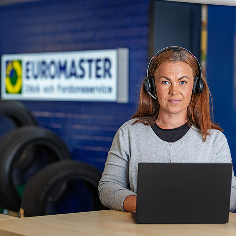 Medarbetare från Euromaster med headset, sittande vid en laptop i kundmottagningen, fotograferad för företagsfotografering.